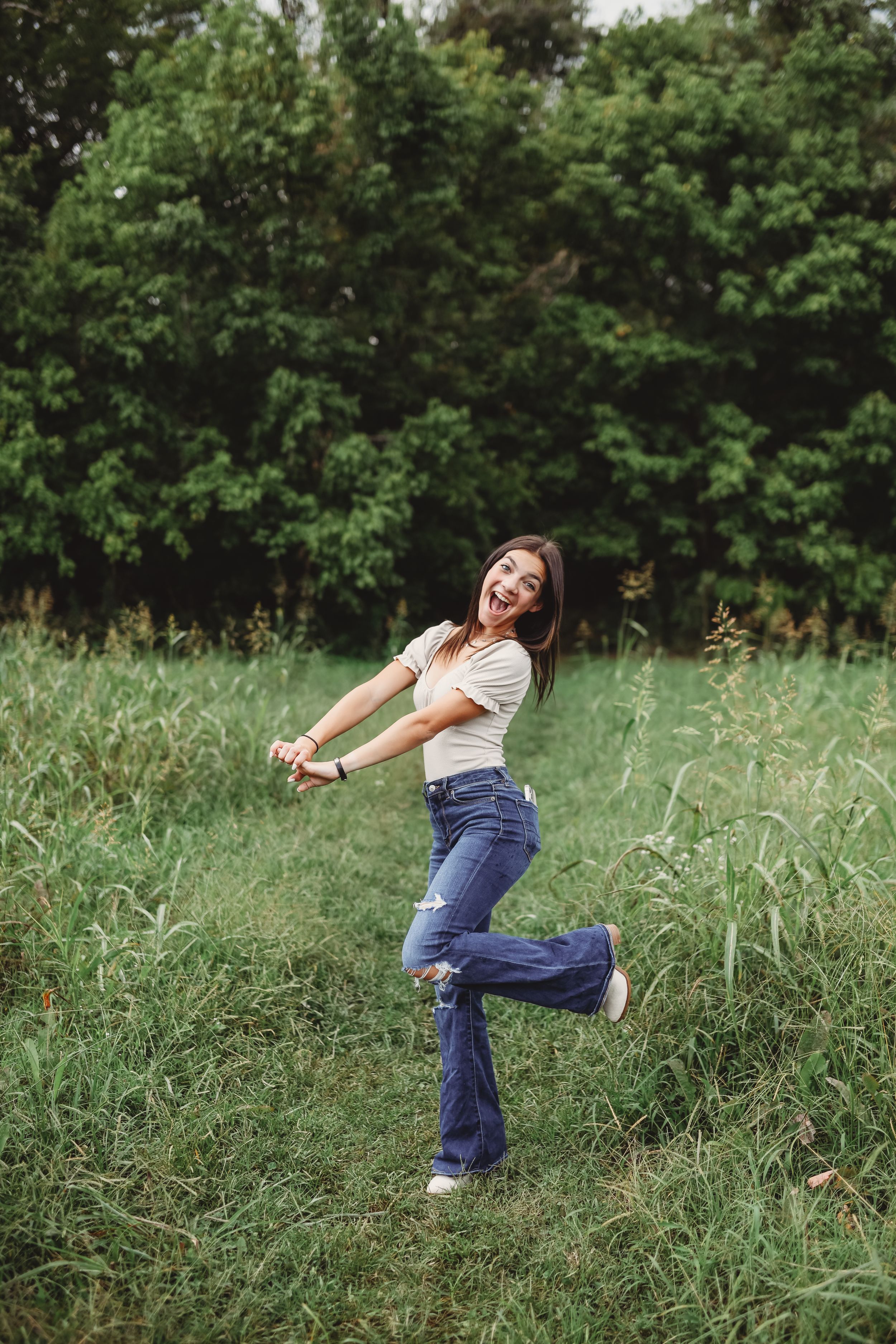 A woman in jeans and white top strikes a playful pose in a grassy field.