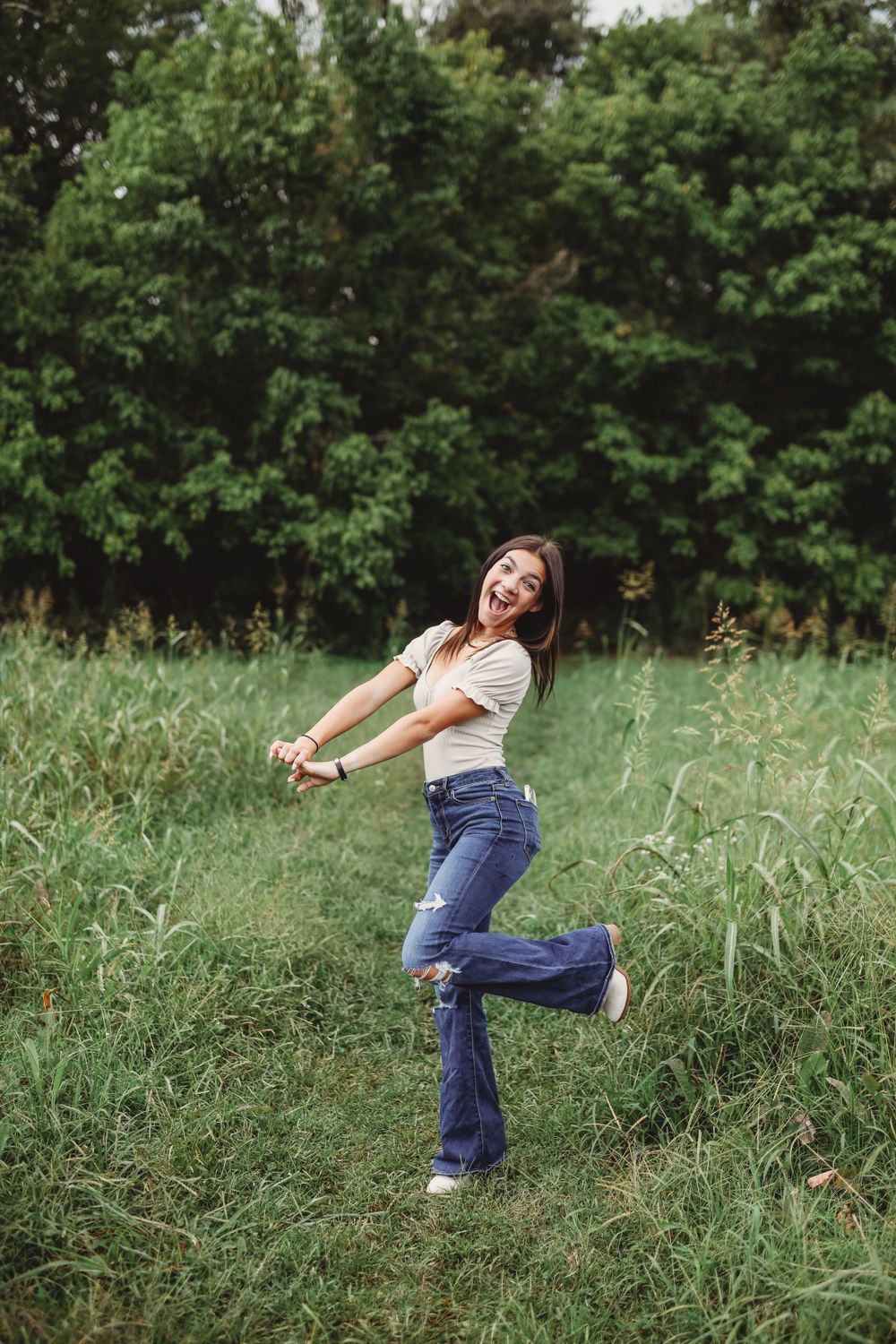 A woman in jeans and white top strikes a playful pose in a grassy field.