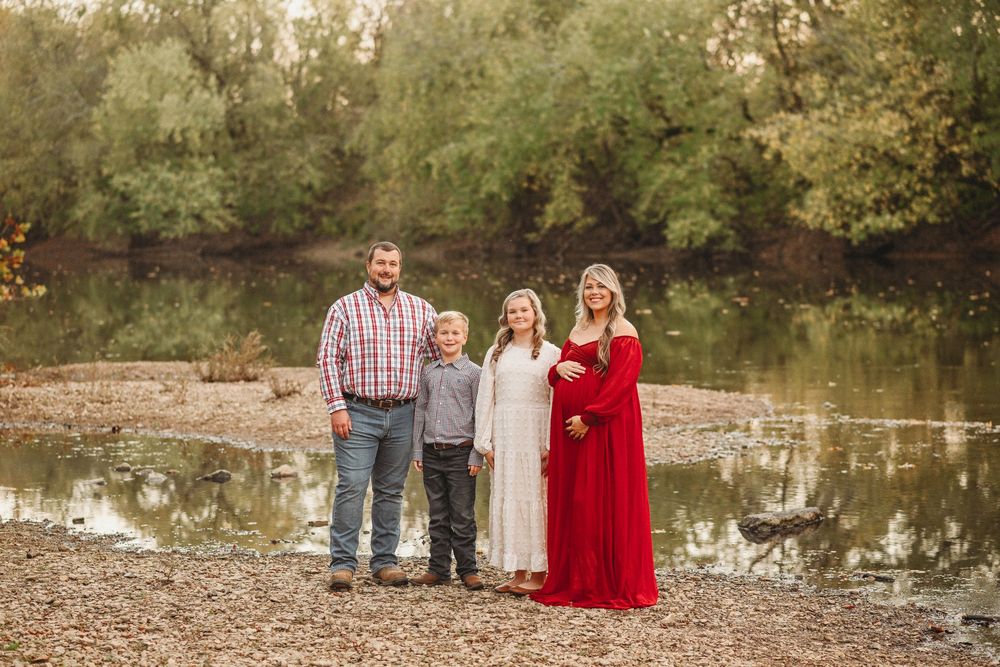 Family portrait session at sunset near a serene pond with autumn trees in the background.