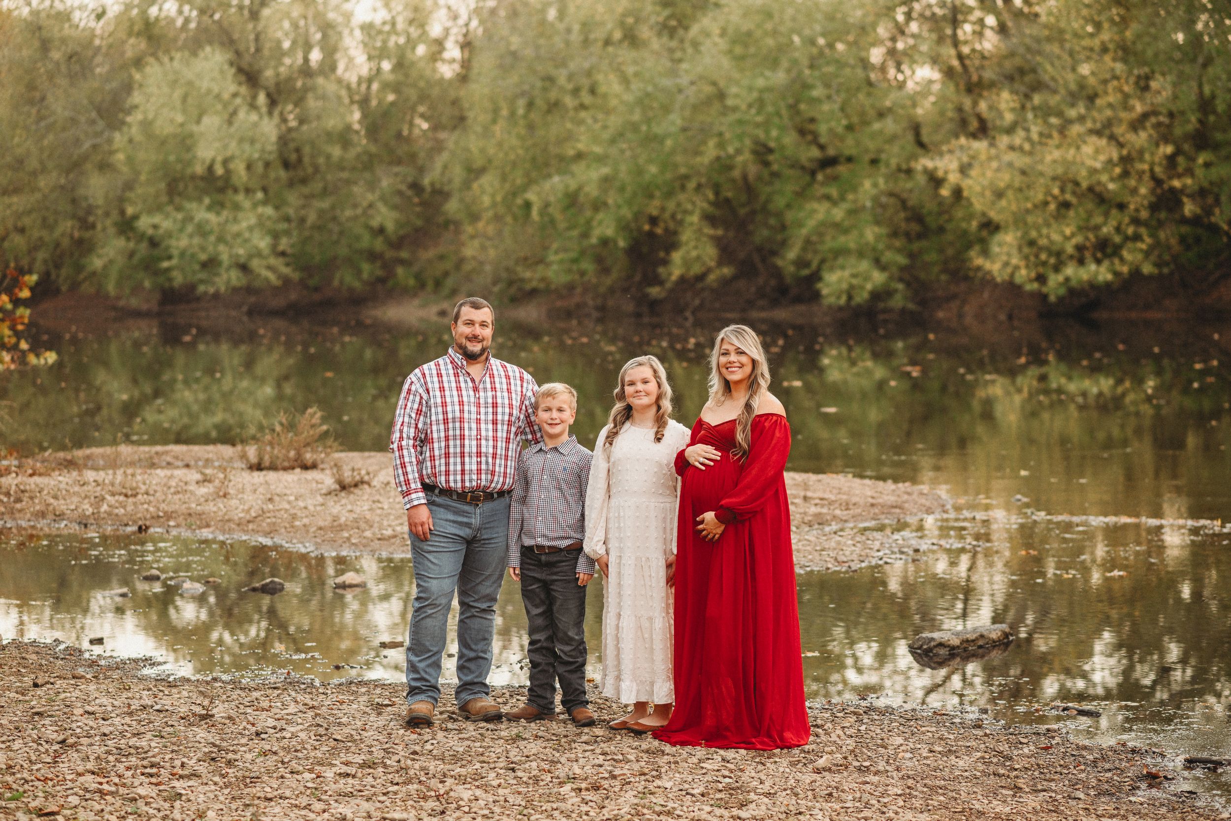 Family portrait session at sunset near a serene pond with autumn trees in the background.