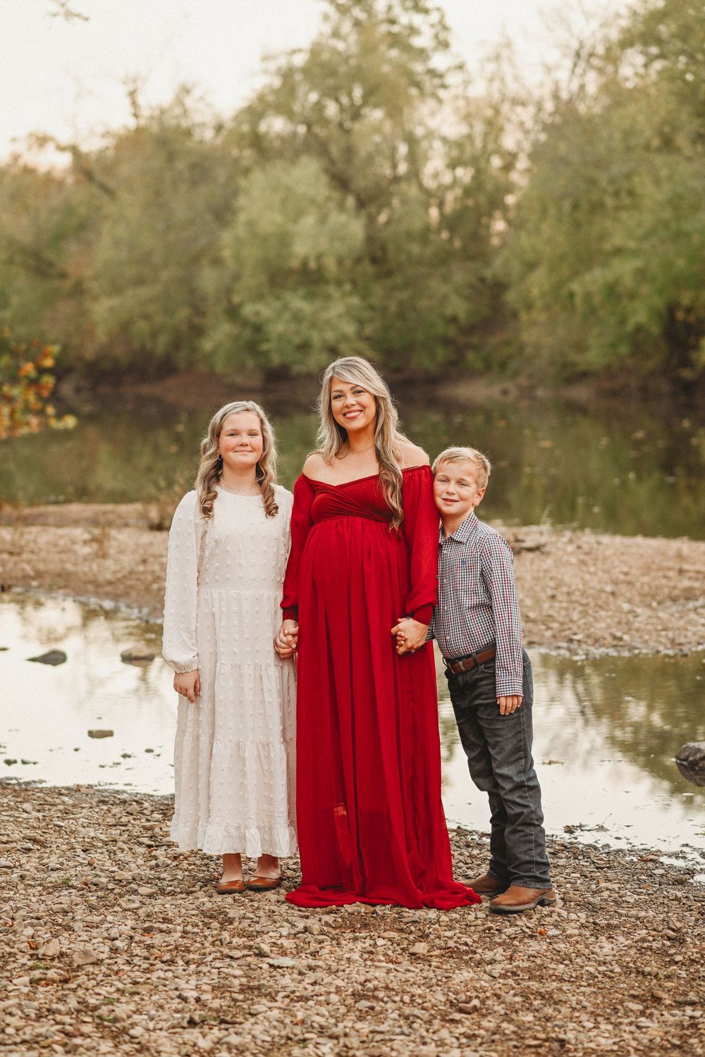 People wearing red and white dresses pose together by a waterside during golden hour.