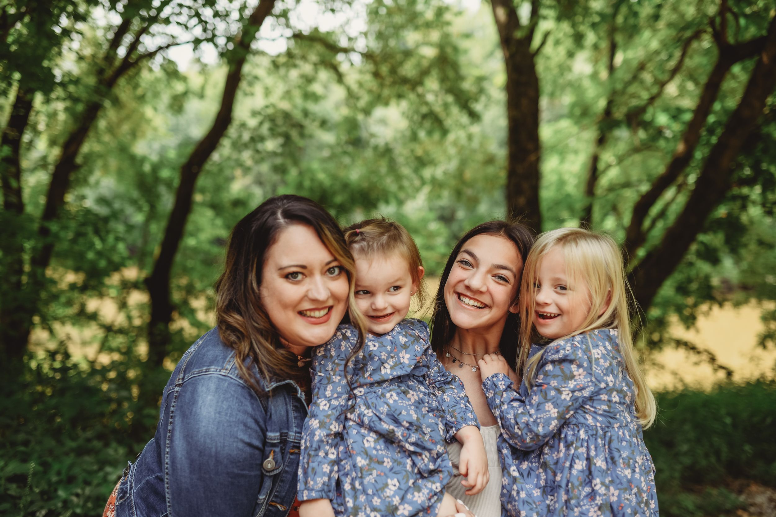 A group poses together wearing coordinating blue outfits in a wooded setting.