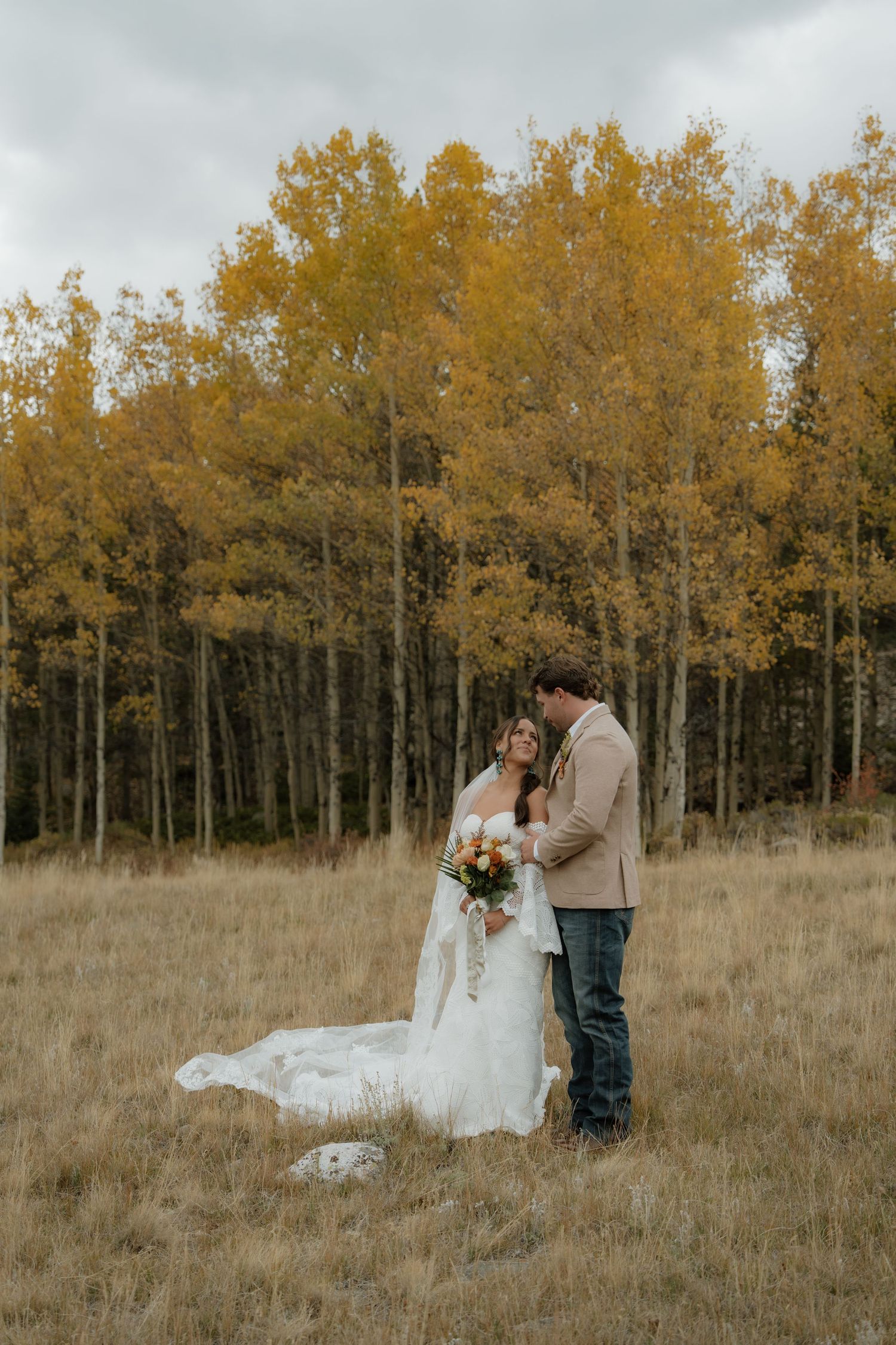 A couple embraces on a hillside with golden aspen trees creating a stunning autumn backdrop in the mountains.