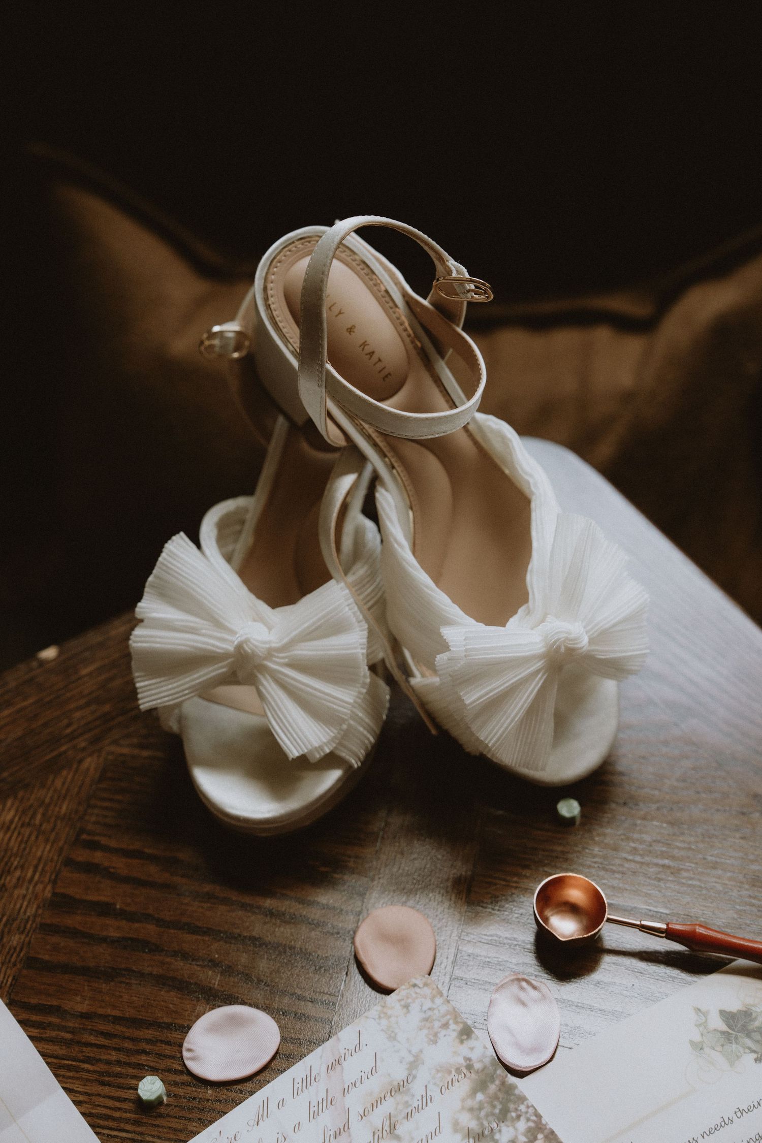 A series of white bridal shoes with delicate bows and tulle details arranged on a wooden surface.