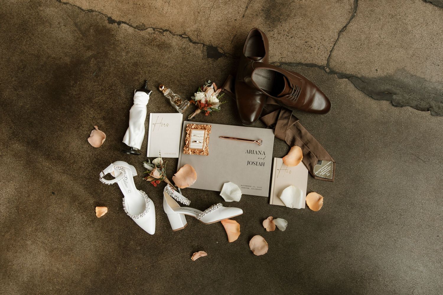 Flat lay of stationery items and dried roses arranged on concrete floor with natural lighting.