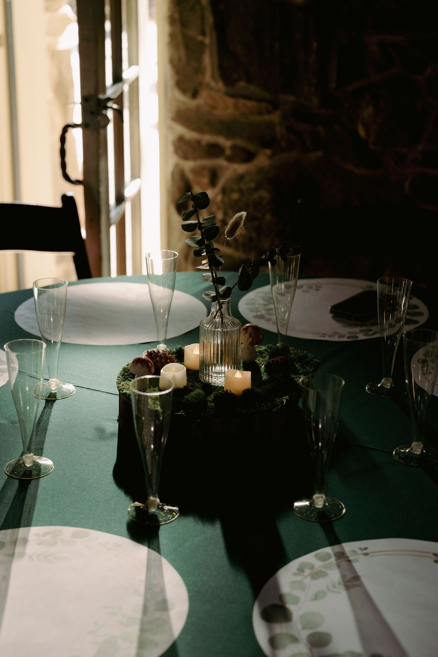 Place settings with glassware and plates arranged on a dark green tablecloth in an elegant dining setup.