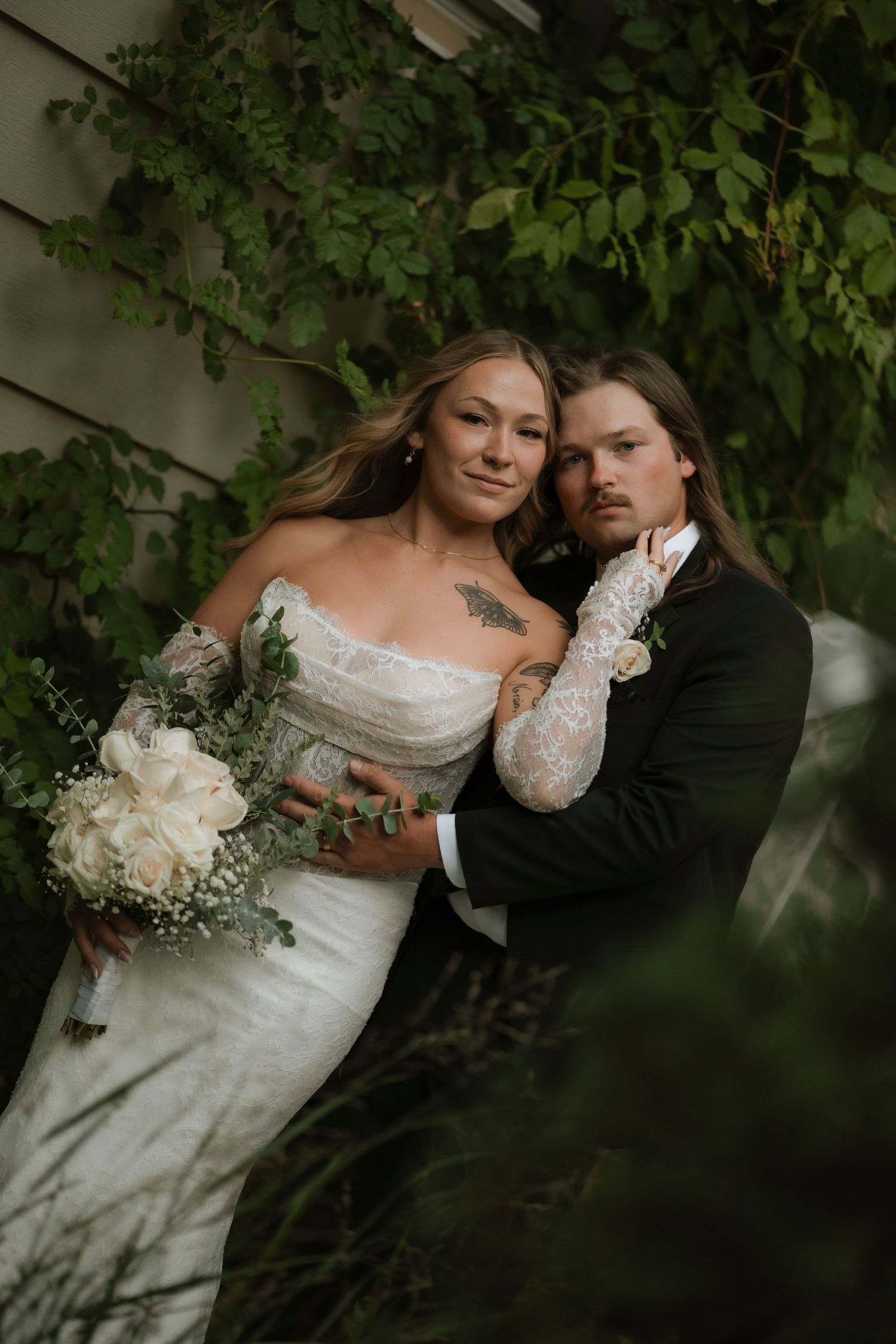 Romantic wedding couple embraces among lush green vines in an intimate garden setting.