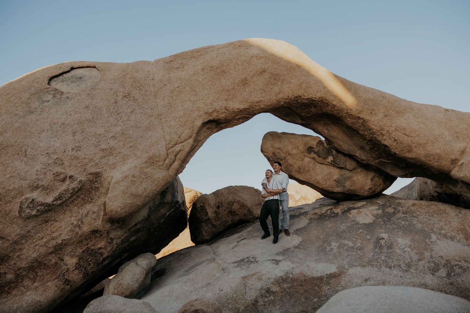 Person standing under natural rock arch formation in desert landscape.