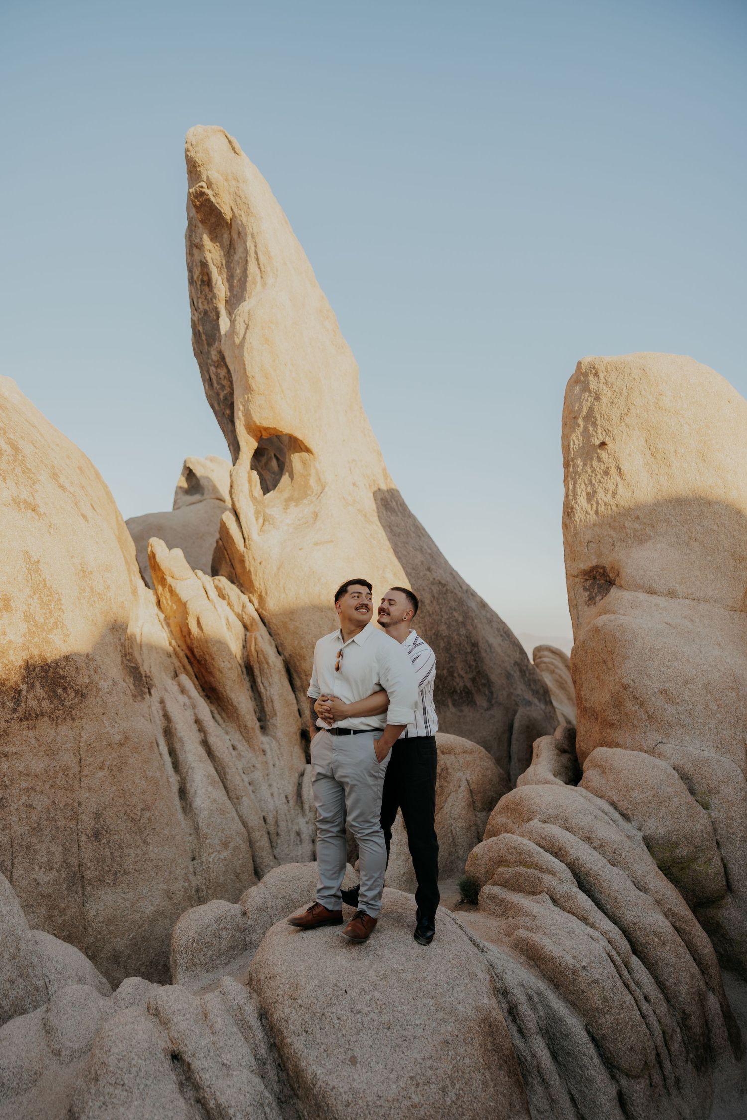 Two people posing among large rock formations in Joshua Tree National Park.