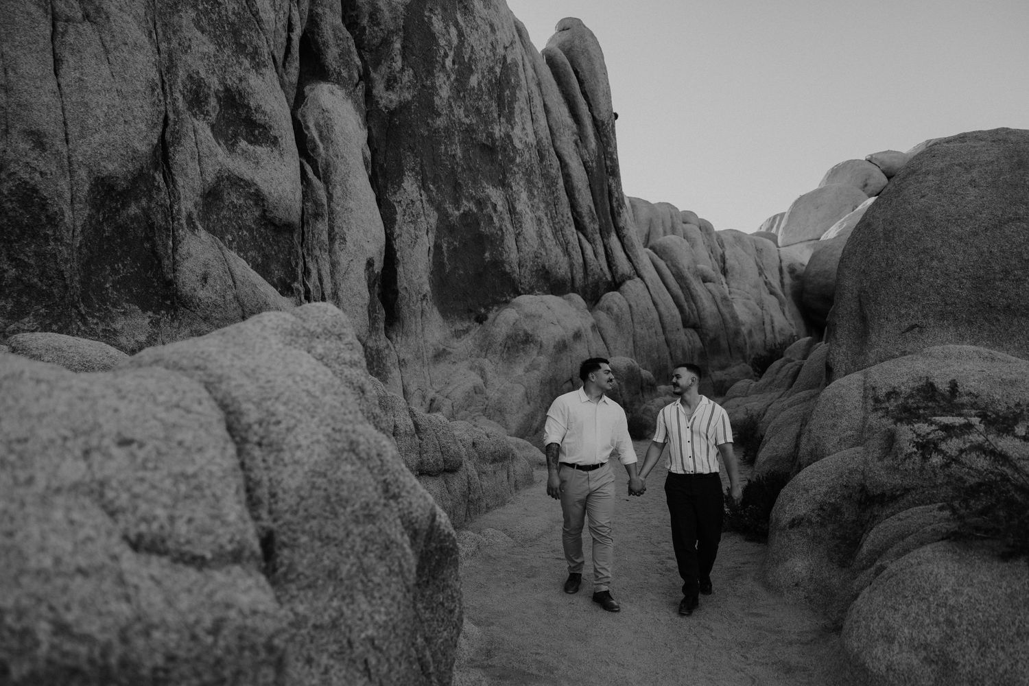 Two people walking together through a dramatic rocky desert landscape with tall boulders.