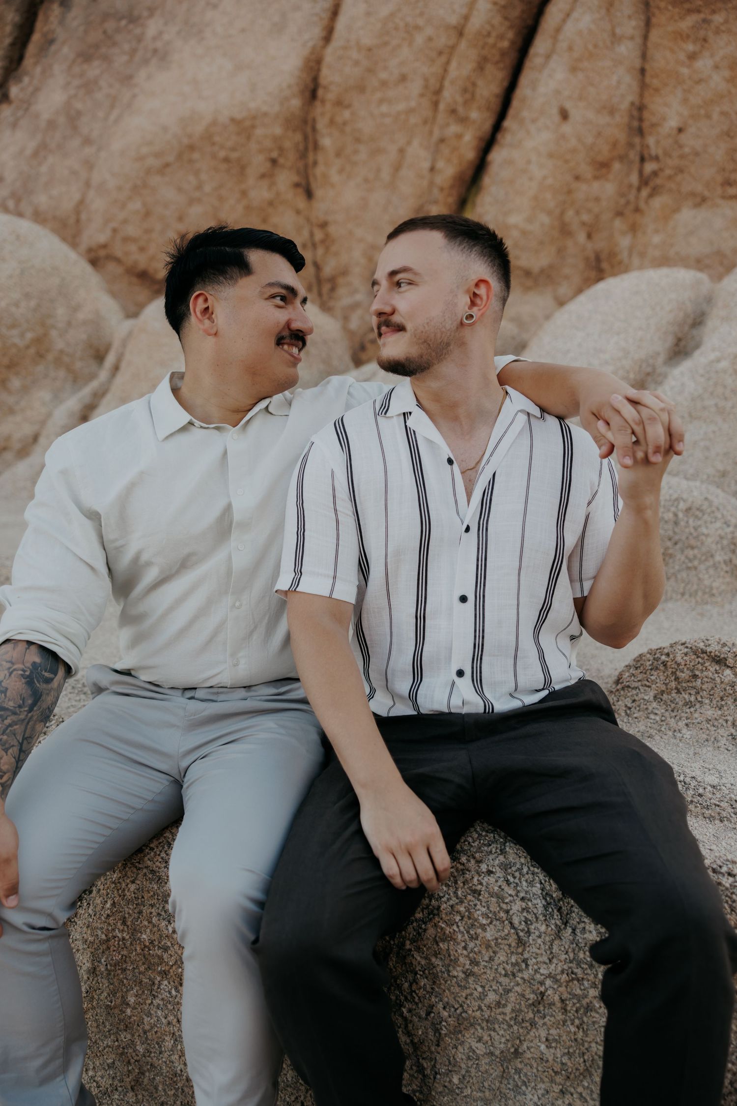 Two people in light colored shirts sitting close together on desert rocks.