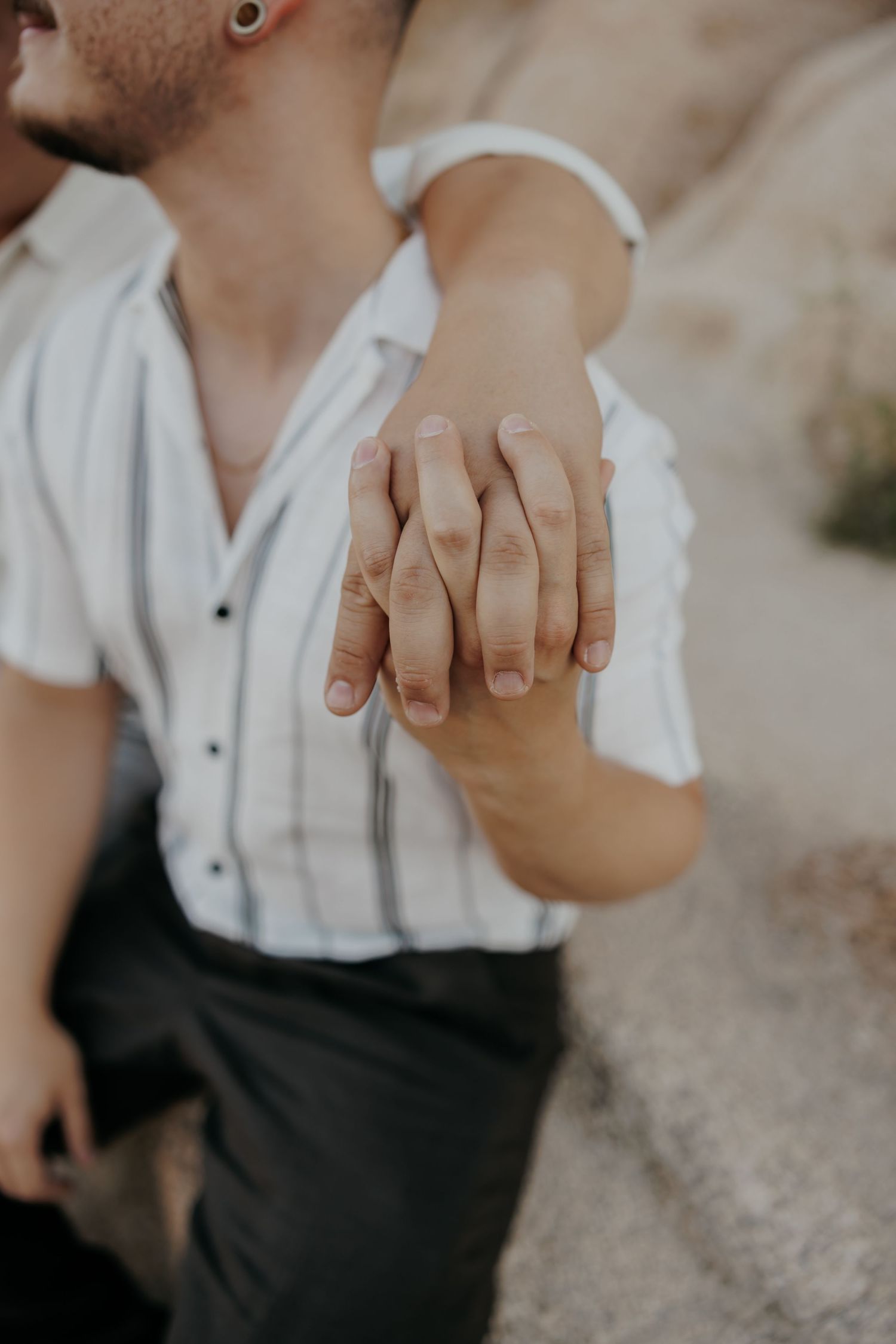 Close-up shot of two hands tenderly clasped together against a desert backdrop.