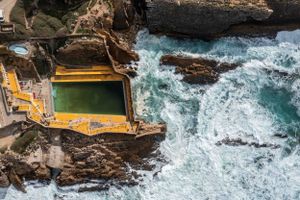 Ocean pool carved into rocky coastline with dramatic crashing waves.