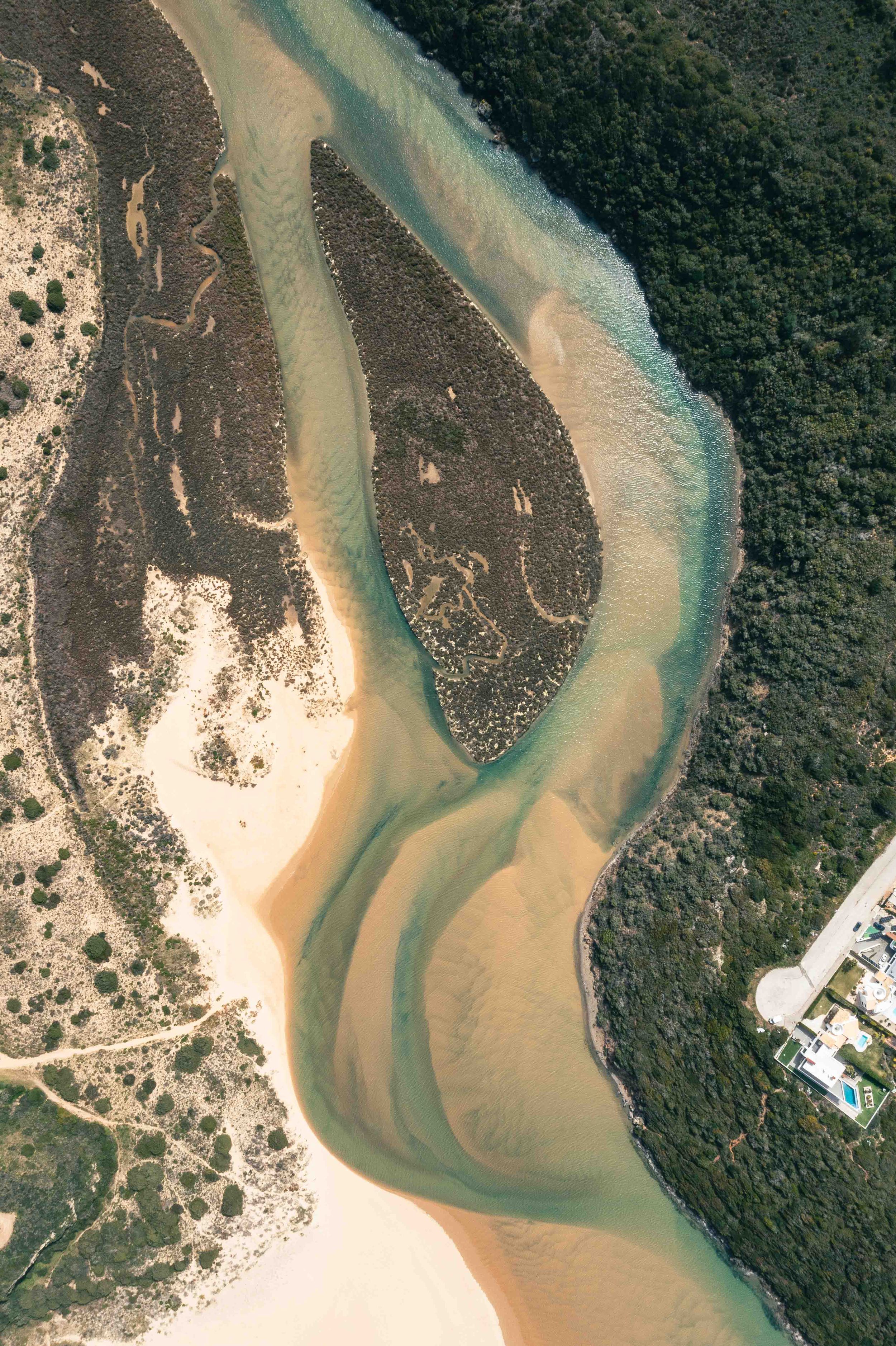 Aerial view of winding coastal river creating patterns in sandy landscape.
