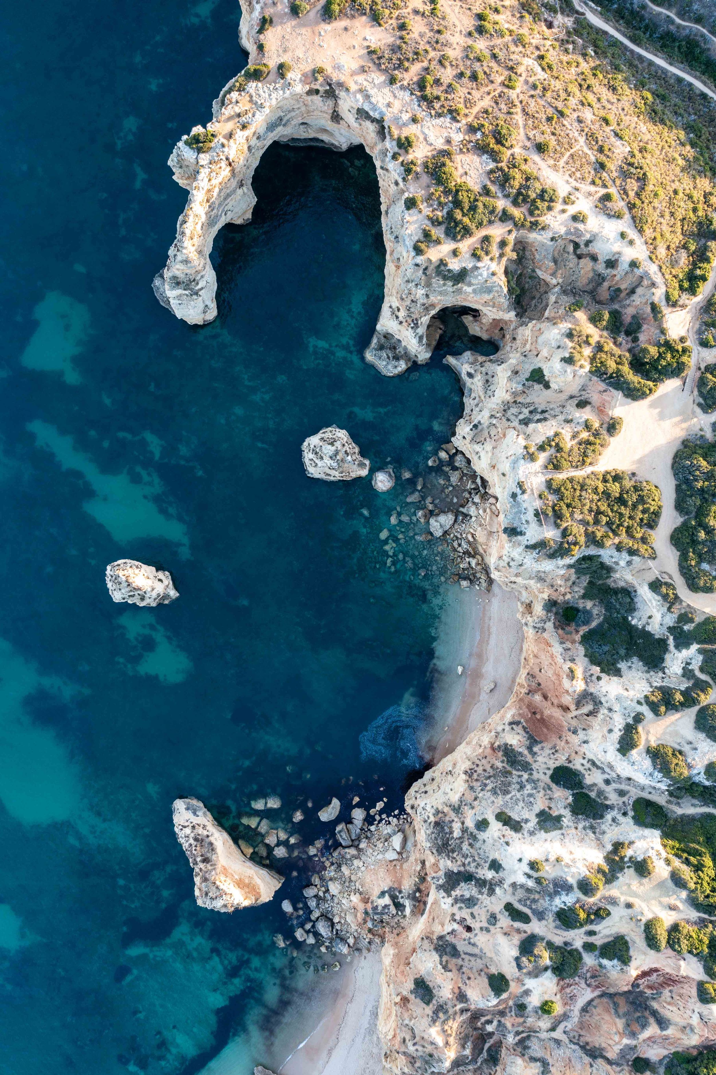 Aerial view of dramatic coastal rock formations and small beaches along turquoise waters.