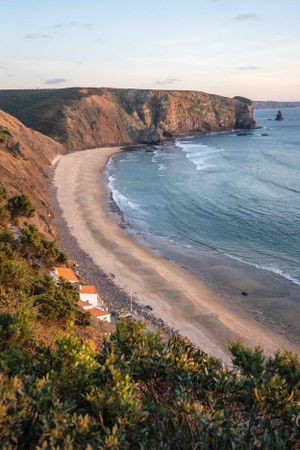 Scenic coastal beach cove with dramatic cliffs and small white house in Portugal.