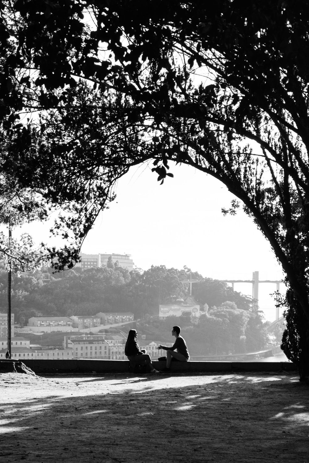 Silhouette of two people sitting under a stone archway overlooking Porto city and bridge in Portugal.