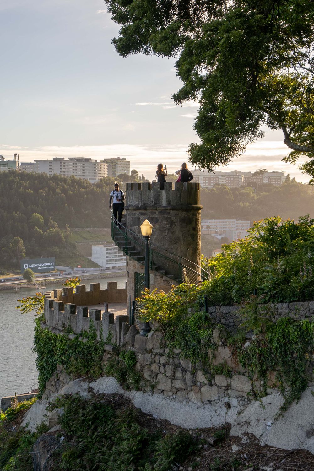People exploring historic stone walls at sunset overlooking coastal city views in Porto.