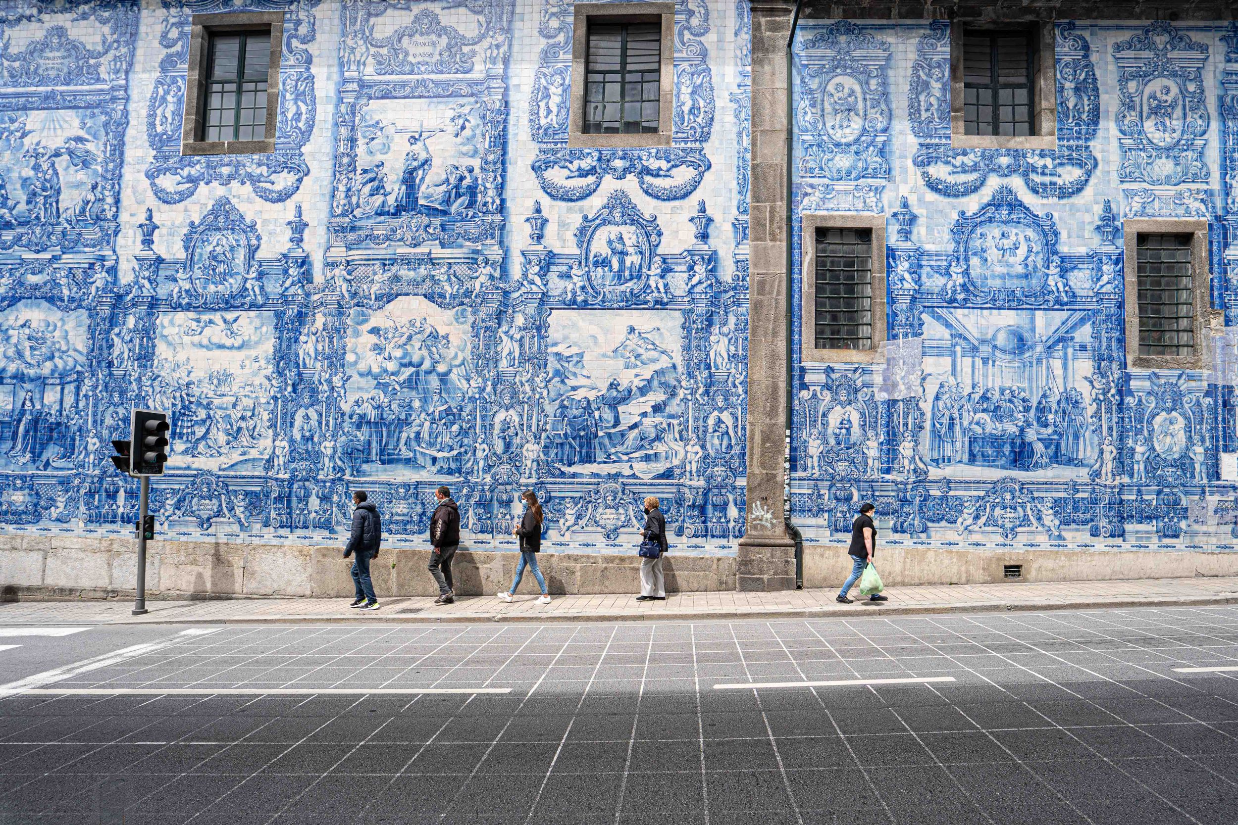 Traditional blue and white Portuguese azulejo tile facade with pedestrians walking past in Porto.
