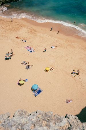 Aerial view of beachgoers relaxing with umbrellas on sandy Portuguese beach.