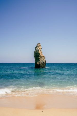 Iconic limestone sea stack rising from turquoise waters at Praia da Marinha beach.