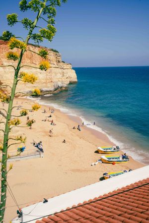 Beach scene with boats and sunbathers beneath limestone cliffs in the Algarve.