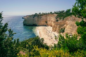 Scenic view of a secluded beach cove surrounded by tall limestone cliffs and blue ocean waters in Portugal.