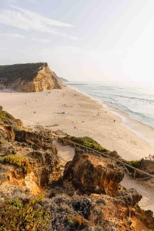 Elevated view of a golden sandy beach nestled between towering coastal cliffs at sunset.