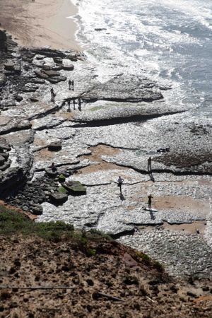Rocky coastal formations with dramatic tidal patterns along a rugged shoreline.