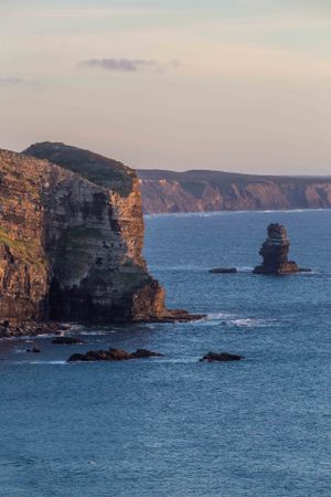 Dramatic coastal cliffs and rock formations jutting into the blue ocean at golden hour.