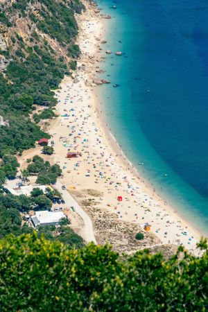 Aerial view of a crowded beach with colorful umbrellas along turquoise Mediterranean waters.