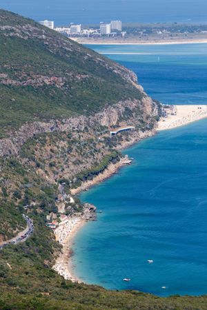 Curved coastline with crystal clear waters and beaches leading to distant city buildings.