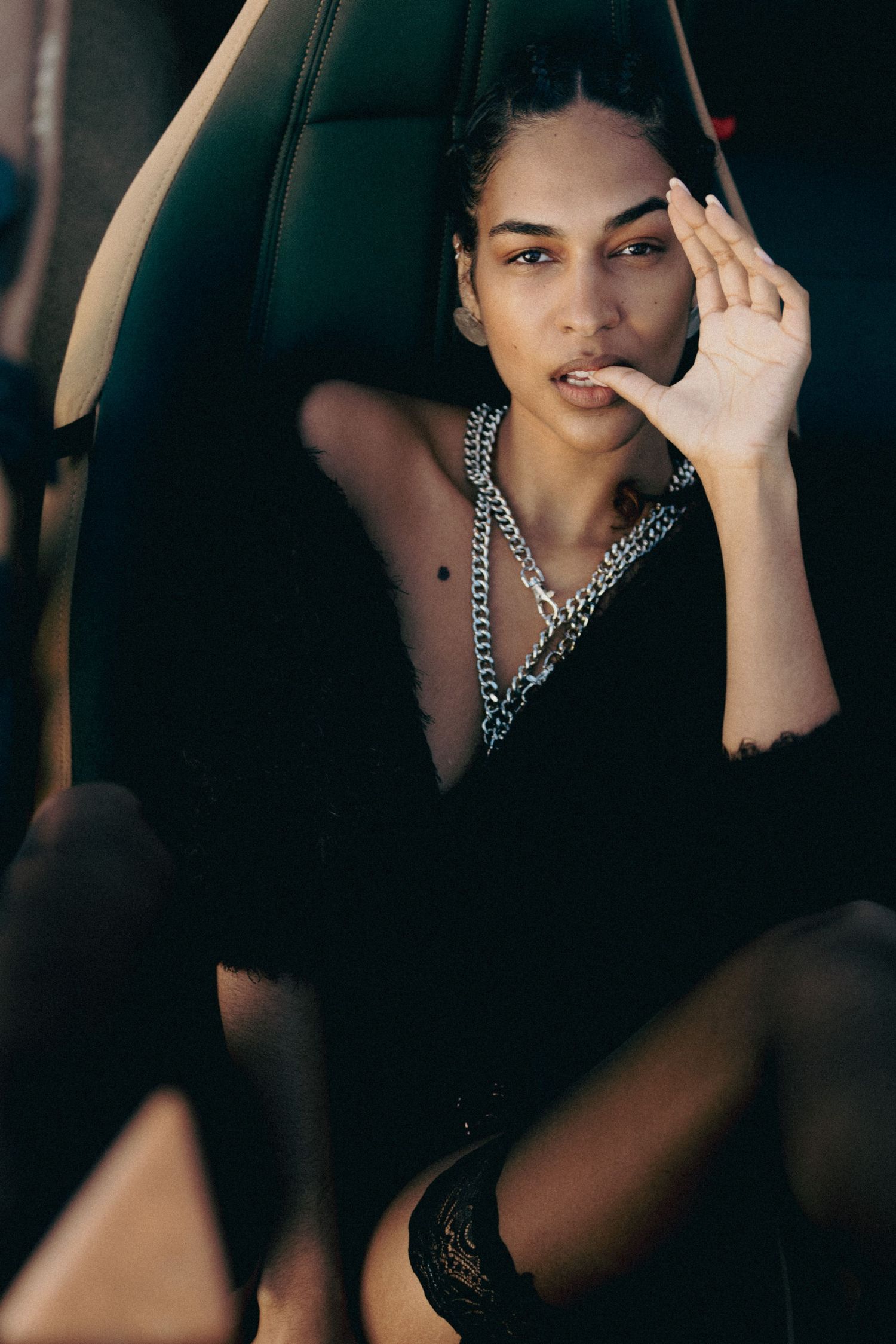 Fashion portrait showing dramatic lighting on model wearing silver chain necklace in dark setting.