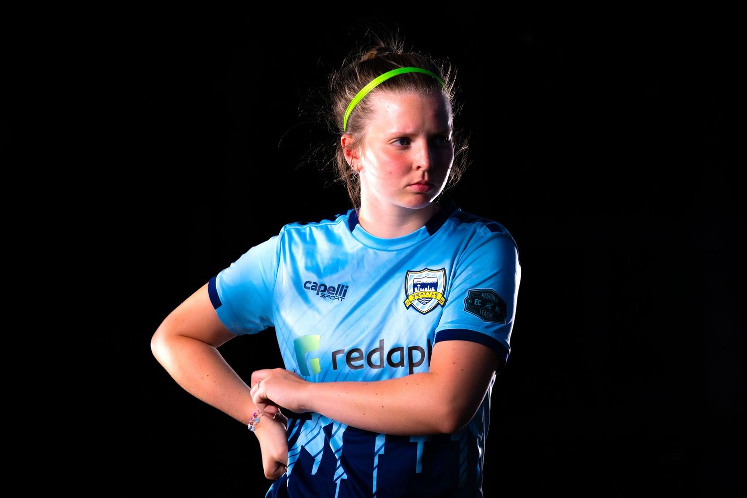 A female soccer player from Seattle United soccer club poses against a dark background.