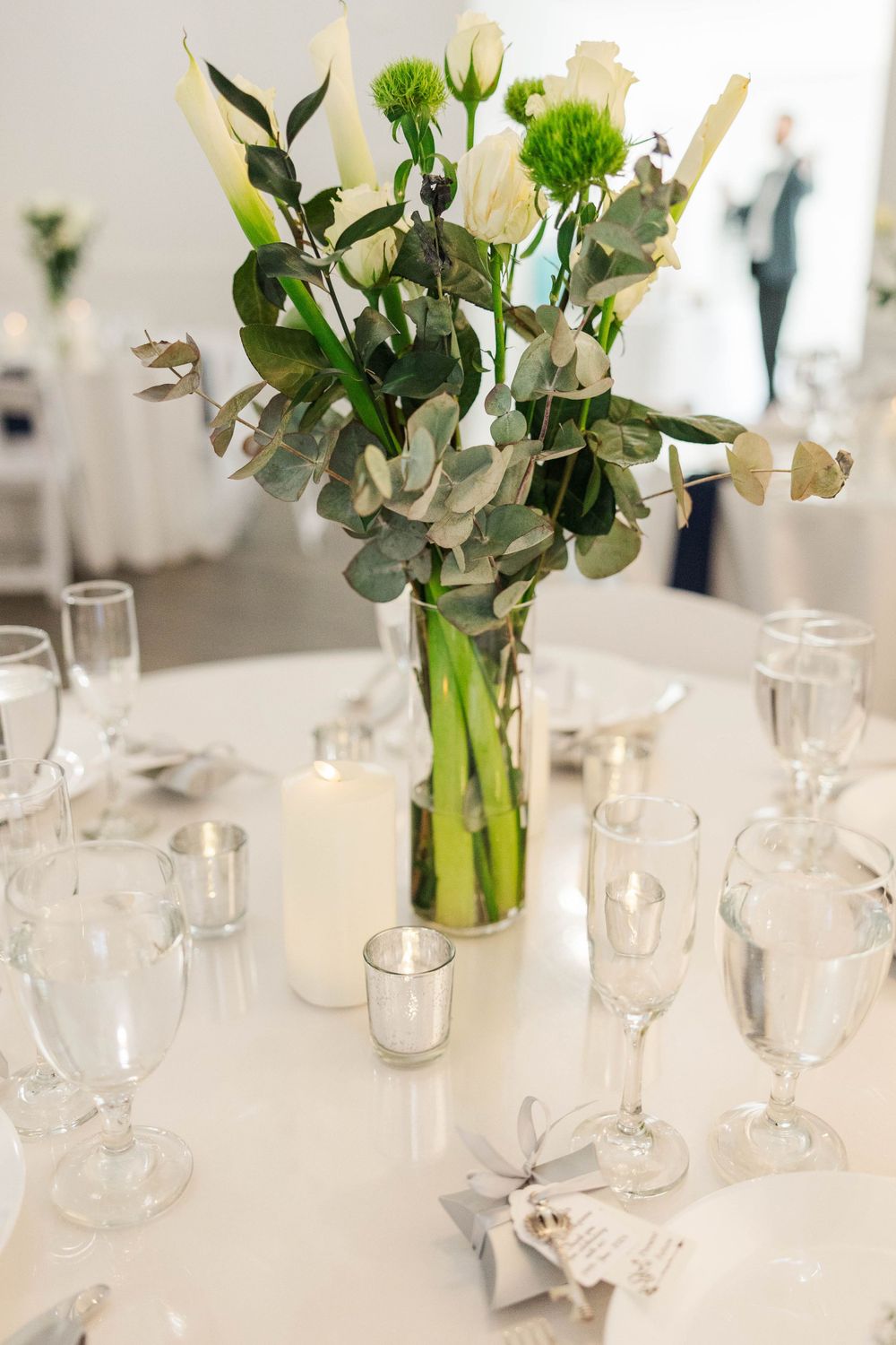 Elegant wedding reception table with white floral centerpiece, candles, and crystal glassware.