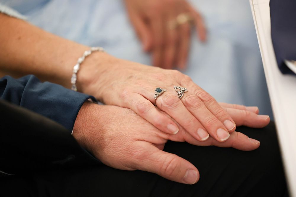 Close-up of two hands touching, wearing rings and bracelet at a wedding ceremony.