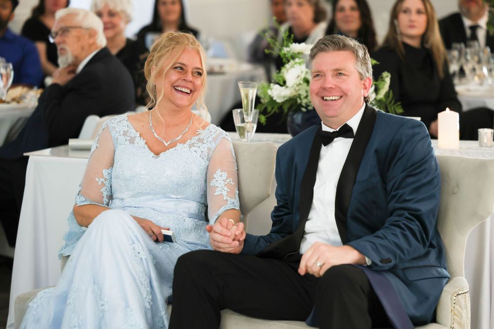 Smiling bride in light blue lace gown and groom in navy tuxedo at wedding reception.