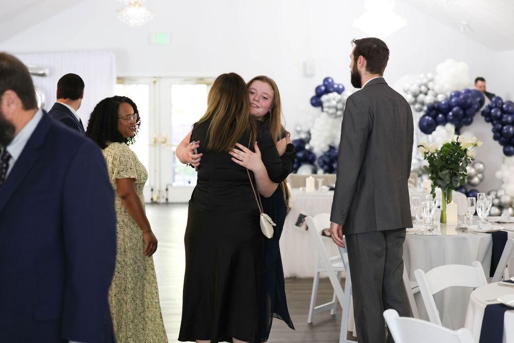 Guests greeting and hugging at an elegant wedding reception with navy balloon arch decor.