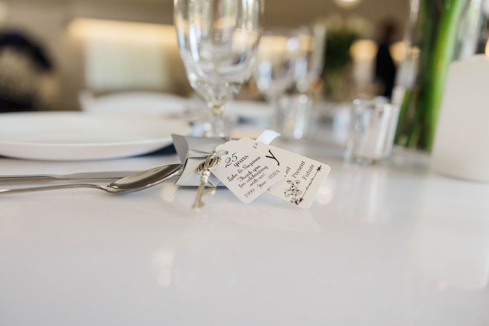 Close-up of wedding place setting with silver key charm and handwritten gift tags on white table.