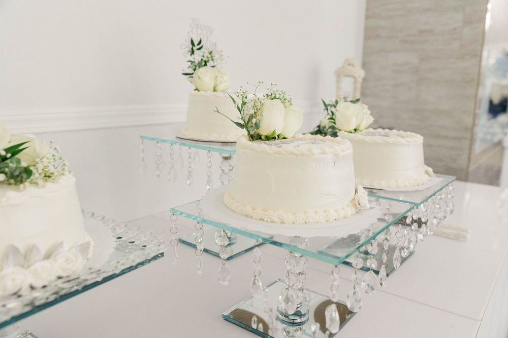 Three white wedding cakes with floral decorations displayed on crystal and mirror cake stands.
