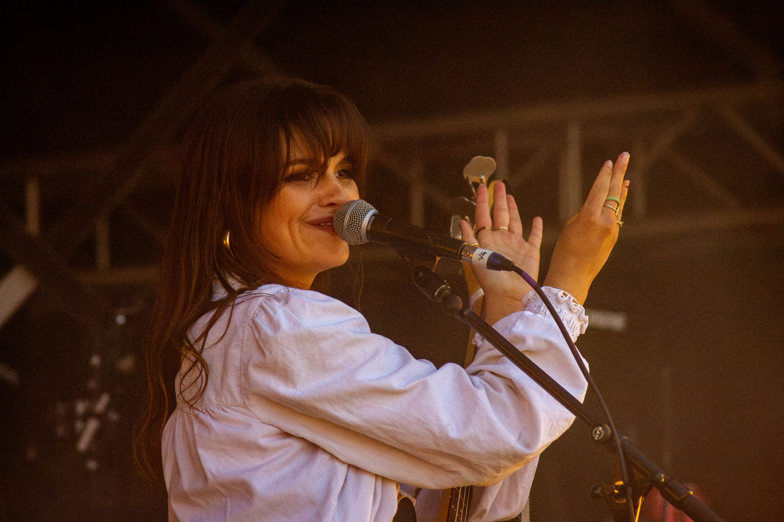 Performer gestures expressively while singing on stage in white blouse.