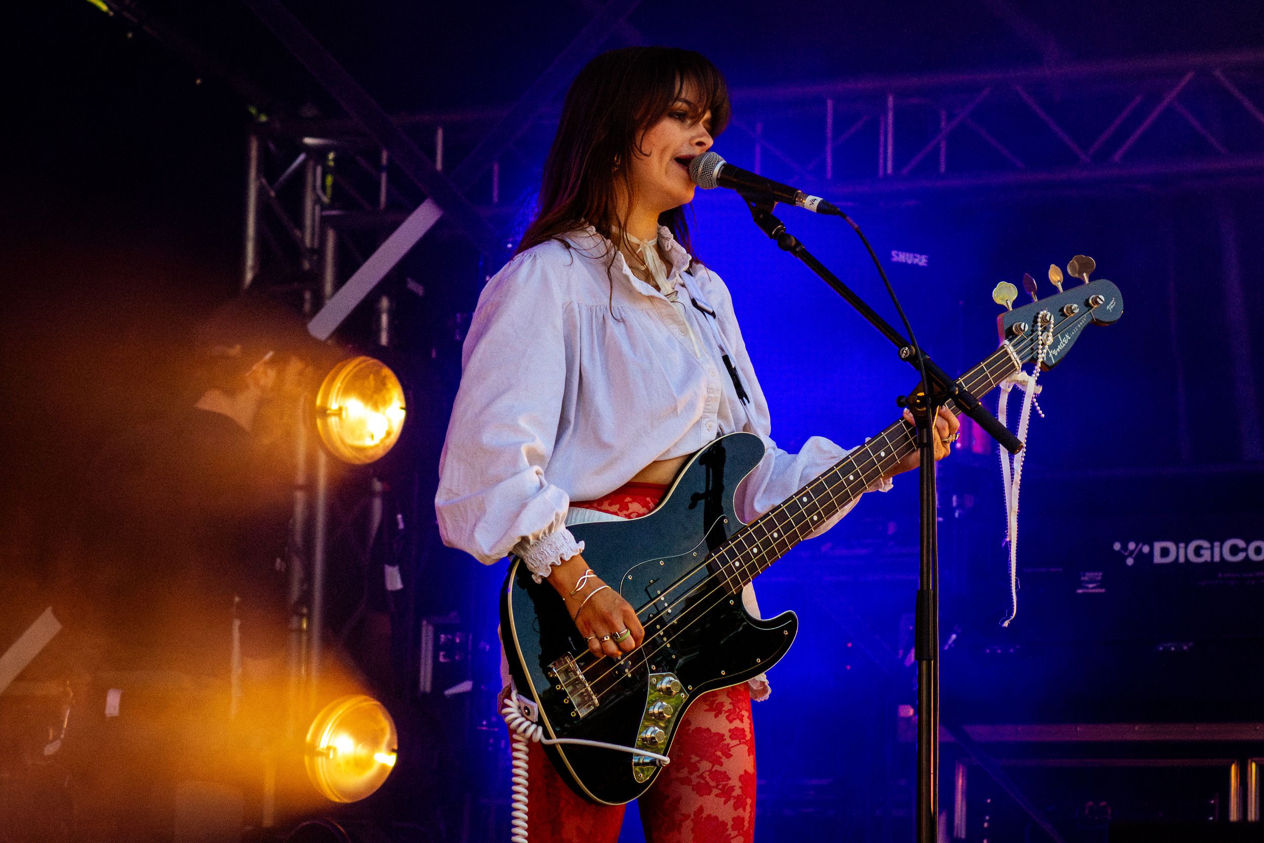 Bass guitarist performs energetically on stage with dramatic orange and blue lighting effects.