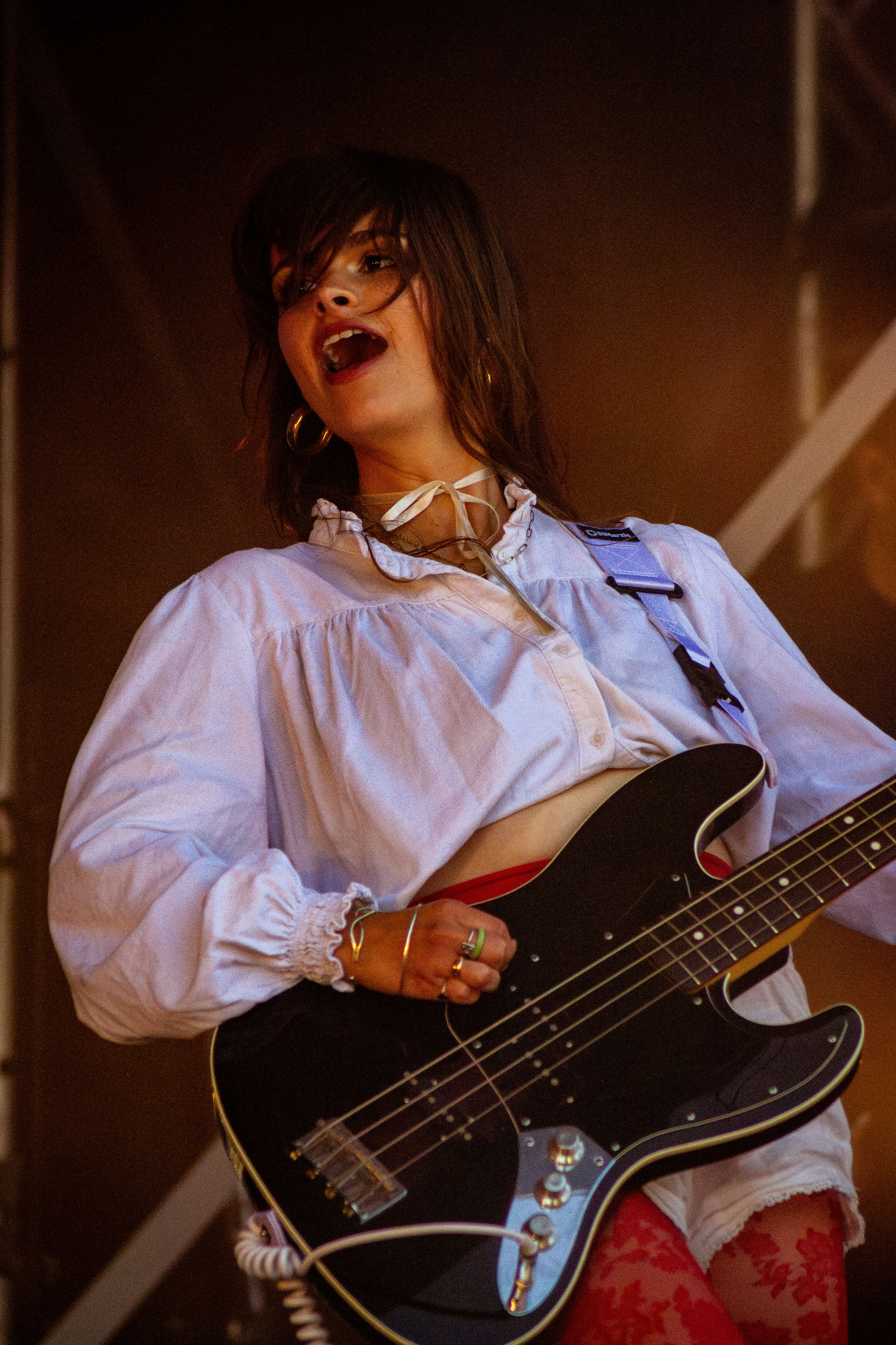 Close-up of musician playing black bass guitar while singing on dimly lit stage.