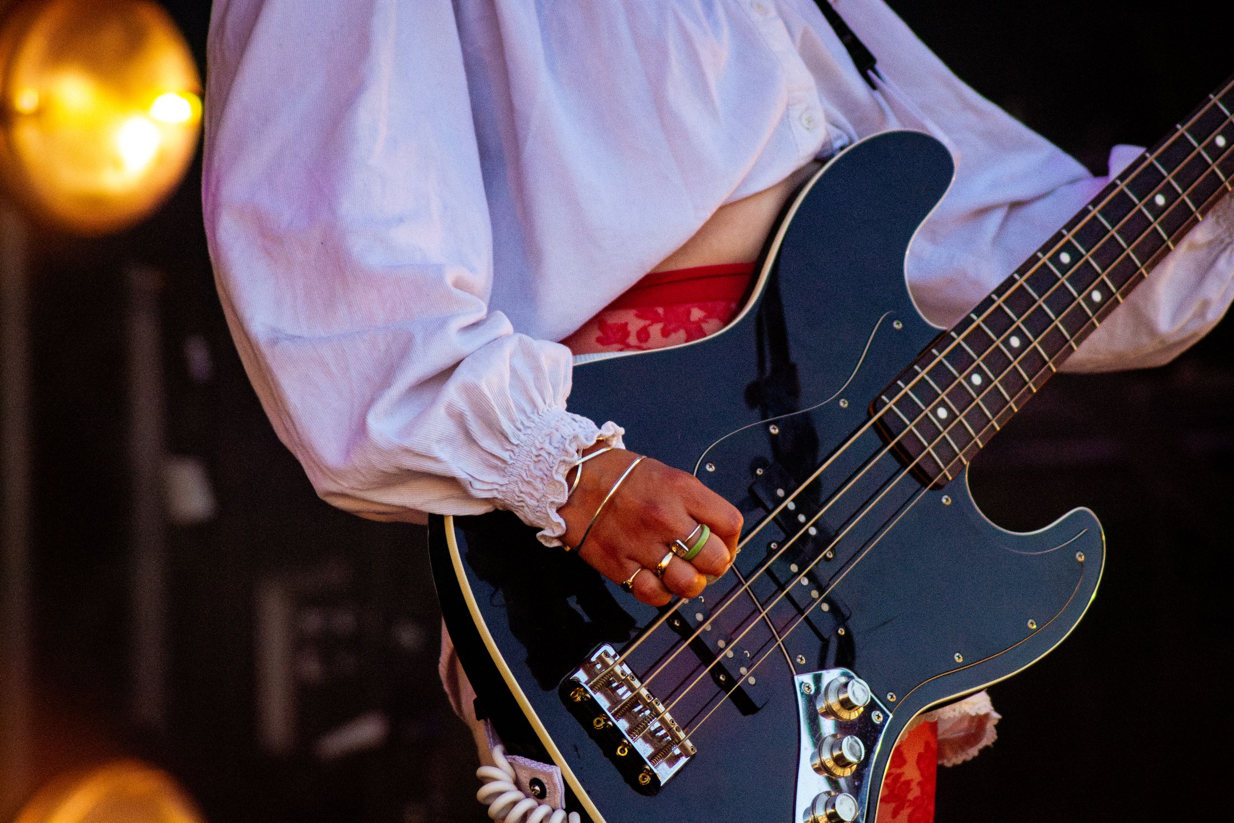 Close-up detail of hands playing blue bass guitar with orange stage lighting.