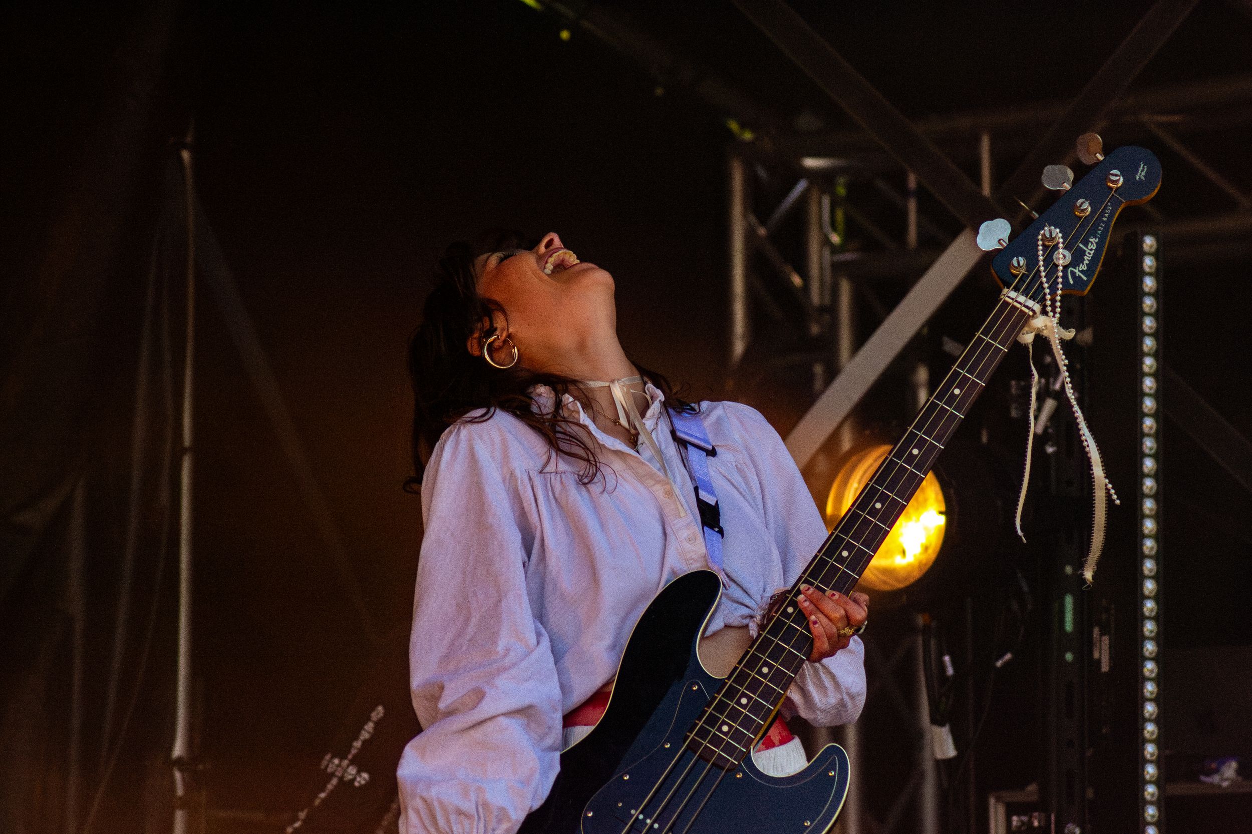 Musician plays bass guitar with dramatic expression under amber stage lighting.