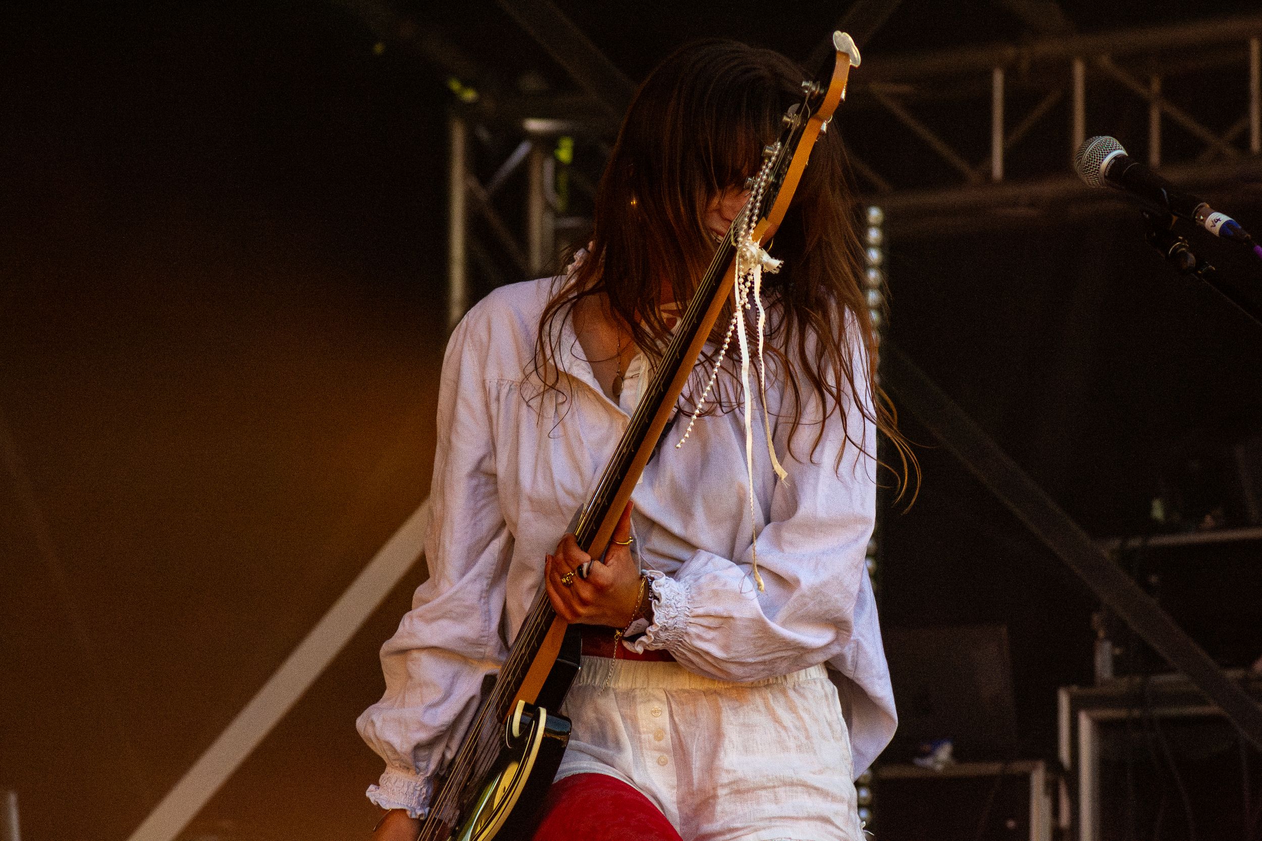 Musician performs on stage with an electric guitar wearing a white shirt and red pants in dramatic lighting.