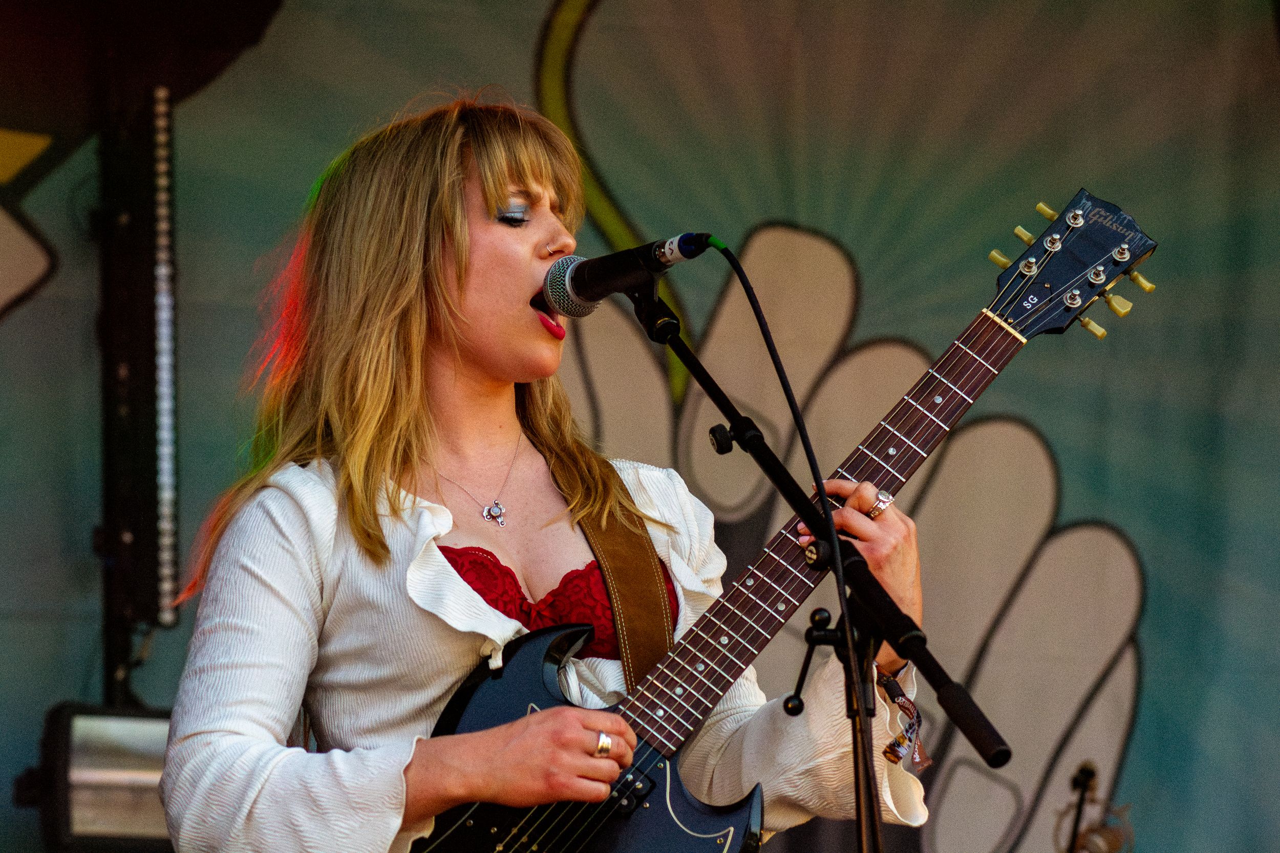 Musician performs with guitar on colorful stage with floral backdrop design.