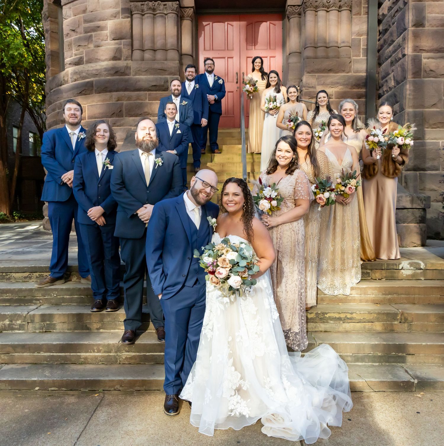 A wedding party portrait in navy blue and champagne attire poses on stone church steps in downtown Birmingham, Alabama.
