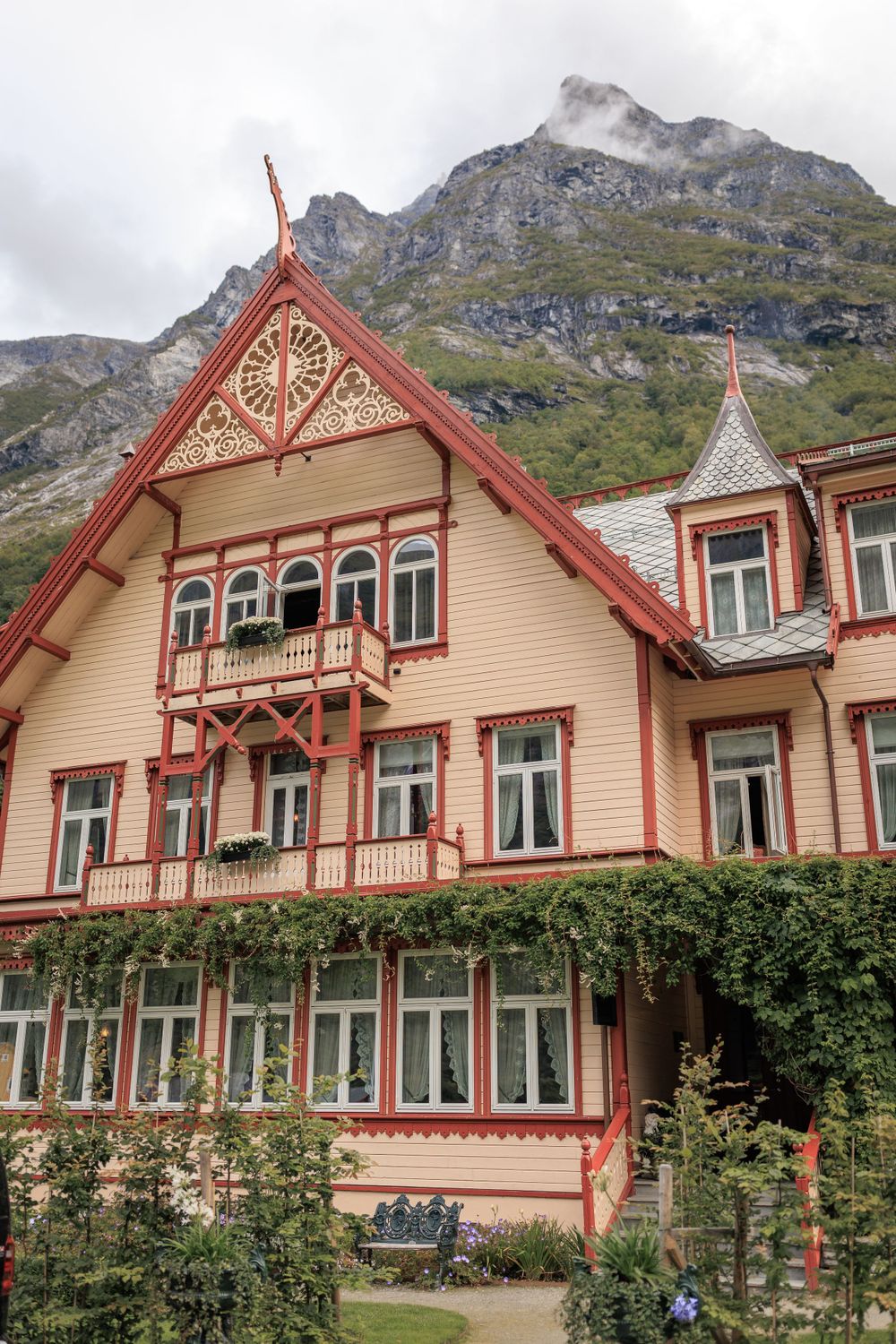 Traditional Norwegian house with decorative peaks and trim against dramatic mountain backdrop.