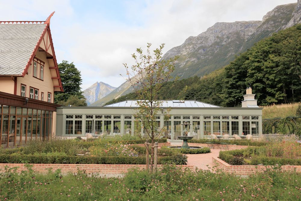 Historic lodge building with glass conservatory nestled against dramatic mountain backdrop.